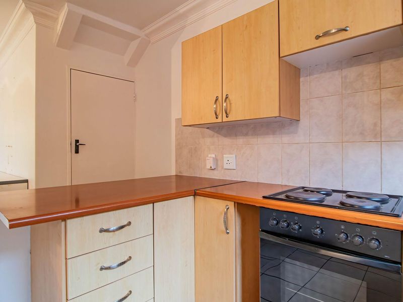 A functional kitchen featuring light wood-finish cabinetry, laminate countertops, and a built-in electric stove and oven with a tiled backsplash.