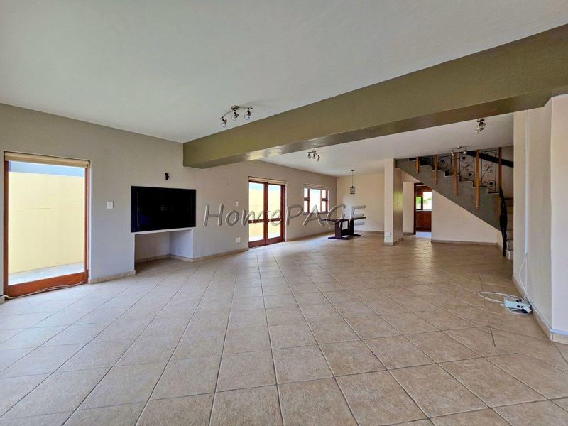 Spacious open-plan living area featuring tiled flooring, a built-in fireplace, and a staircase with decorative wrought iron railings leading to the upper level.