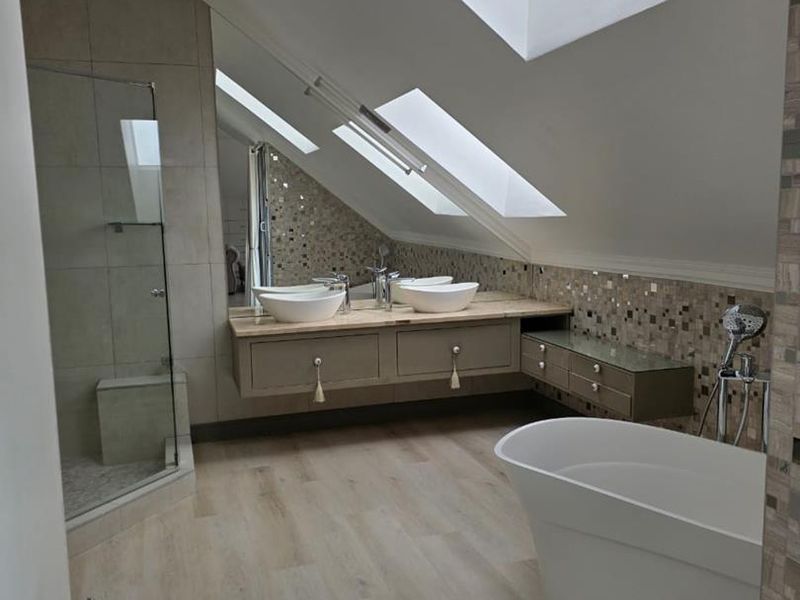 Modern attic bathroom featuring a freestanding bathtub, glass-enclosed shower, double vanity with vessel sinks, and natural light from multiple skylights.
