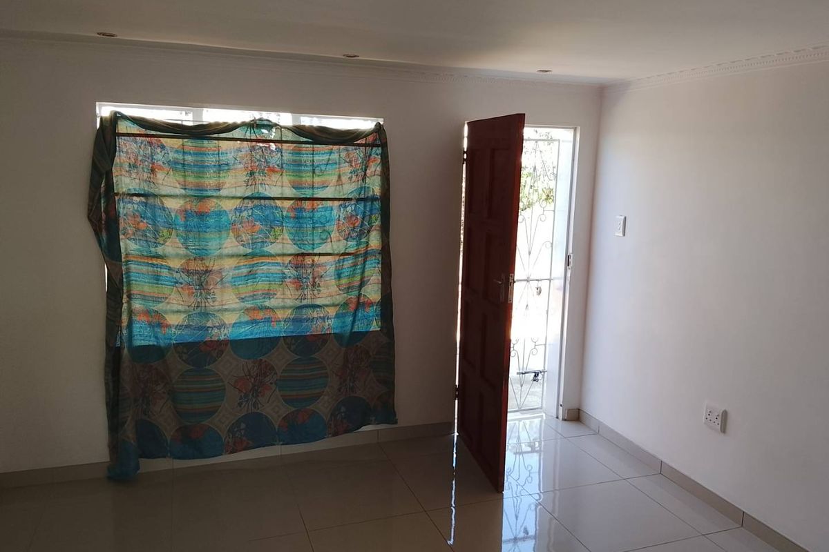 A bright, empty living area featuring neutral tiled flooring, recessed ceiling lights, and direct access to an exterior security gate.