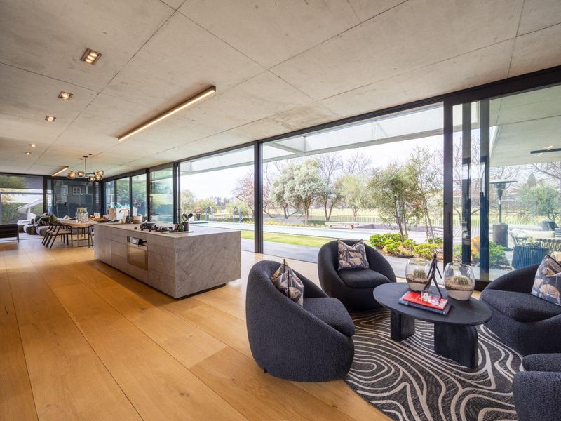 Spacious open-plan living and kitchen area featuring high-end finishes, exposed concrete ceilings, and expansive sliding glass doors opening to the outdoor pool area.