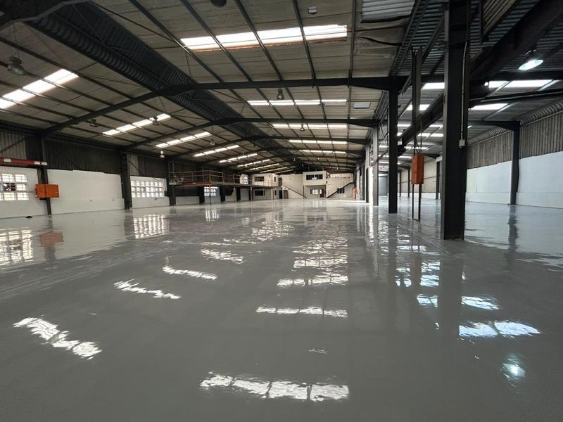 Spacious industrial warehouse featuring a high-gloss epoxy floor, steel portal frame construction, integrated mezzanine level, and ample natural light through overhead skylights.