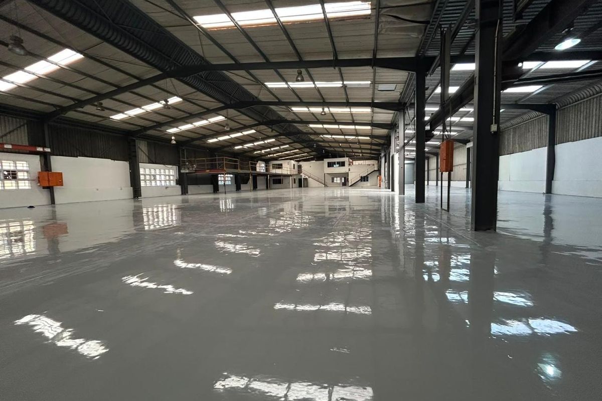 Spacious industrial warehouse featuring a high-gloss epoxy floor, steel portal frame construction, integrated mezzanine level, and ample natural light through overhead skylights.