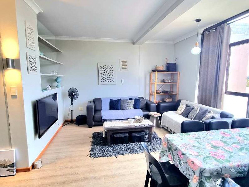 A bright open-plan living and dining area featuring laminate flooring, built-in shelving, and large windows providing ample natural light.
