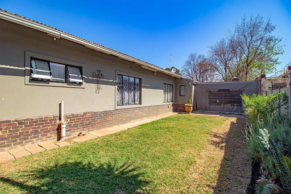 A rear exterior view of the house featuring a brick and plaster facade, lawn area, and a covered patio section.