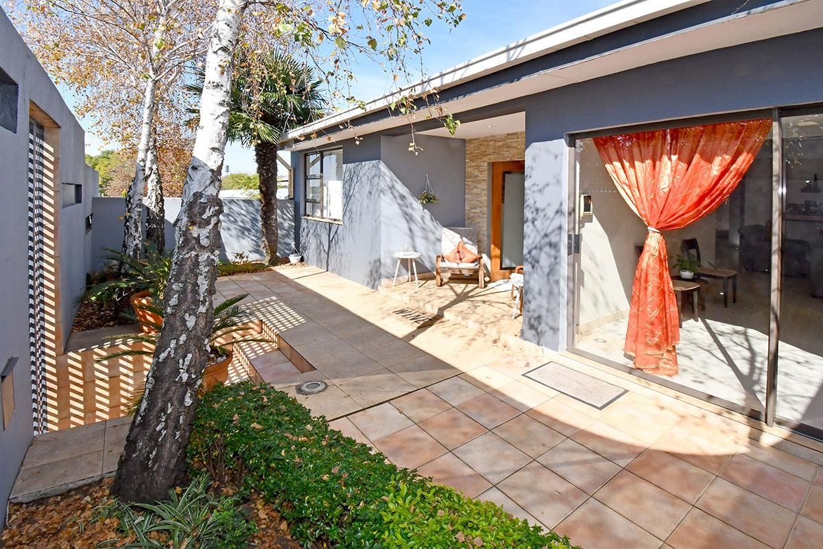 A well-maintained rear patio area featuring tiled flooring, sliding glass doors, and a landscaped garden border with mature trees.