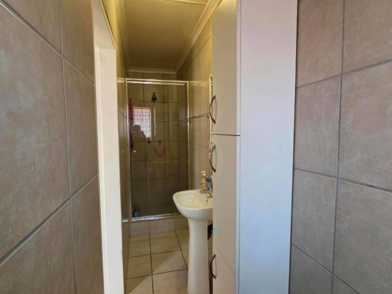 A functional bathroom featuring a pedestal basin, a shower enclosure with glass door, and neutral wall and floor tiling with built-in storage.