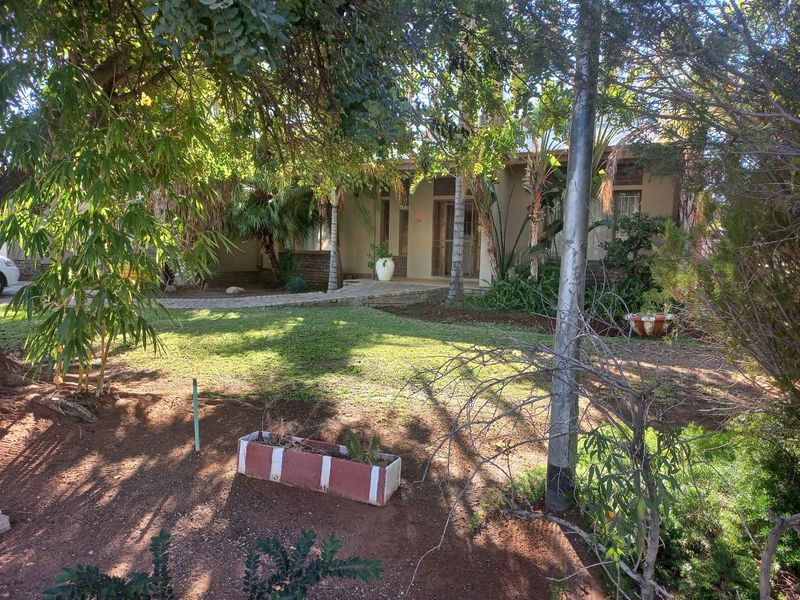 Front view of the property featuring a paved walkway leading to the entrance, surrounded by established trees and a landscaped garden area.