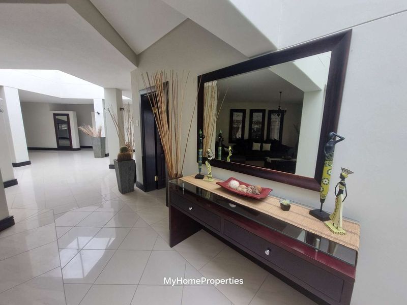 Spacious hallway featuring polished tile flooring, a high recessed ceiling with a skylight, and neutral wall finishes.