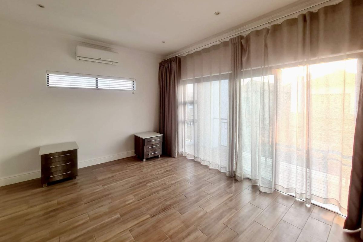 A bright and spacious bedroom featuring wood-look tile flooring, a wall-mounted air conditioning unit, and large sliding glass doors leading to a balcony.