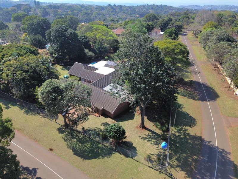 Aerial view of a residential property featuring a tiled roof with solar panels, a swimming pool, and surrounding garden space.
