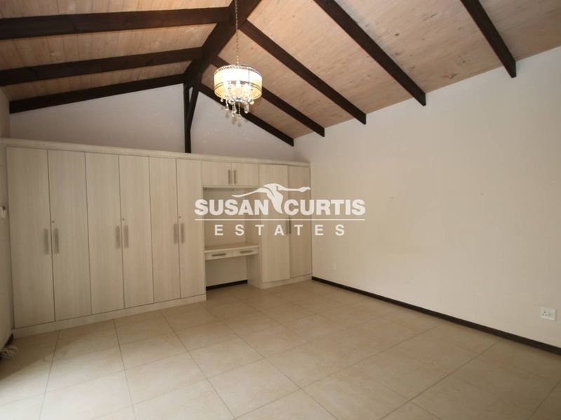Spacious bedroom featuring a vaulted ceiling with exposed timber beams, tiled flooring, and extensive built-in cabinetry with an integrated desk area.