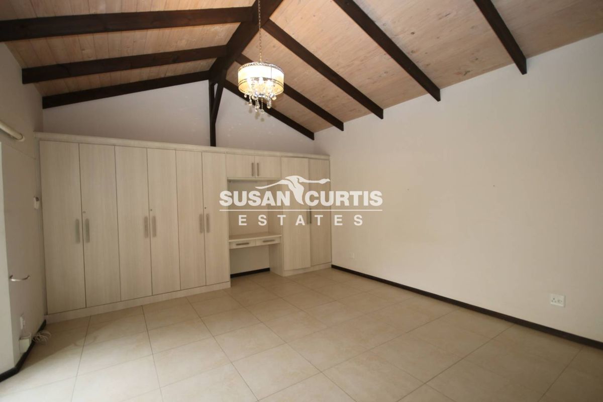 Spacious bedroom featuring a vaulted ceiling with exposed timber beams, tiled flooring, and extensive built-in cabinetry with an integrated desk area.