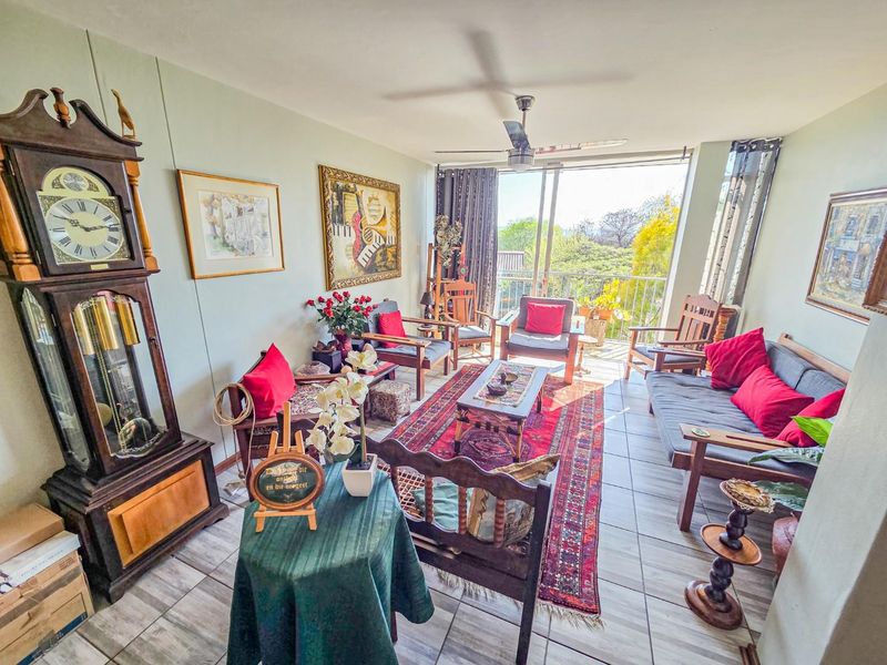 A bright living room featuring tiled flooring, a ceiling fan, and large sliding glass doors providing access to an outdoor balcony area.
