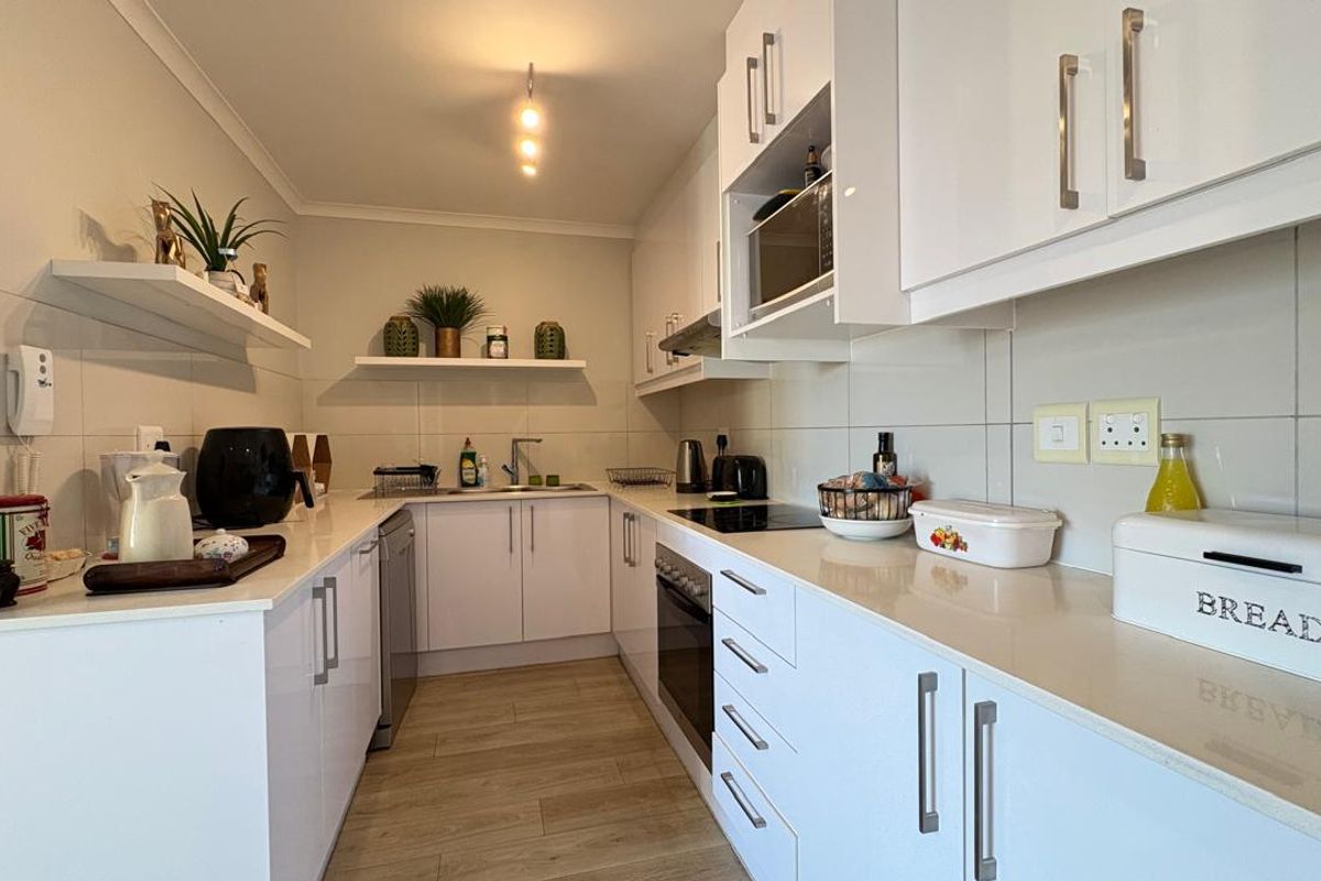 Modern galley-style kitchen featuring white cabinetry, integrated oven, hob, extractor fan, and tiled backsplash with ample counter space.