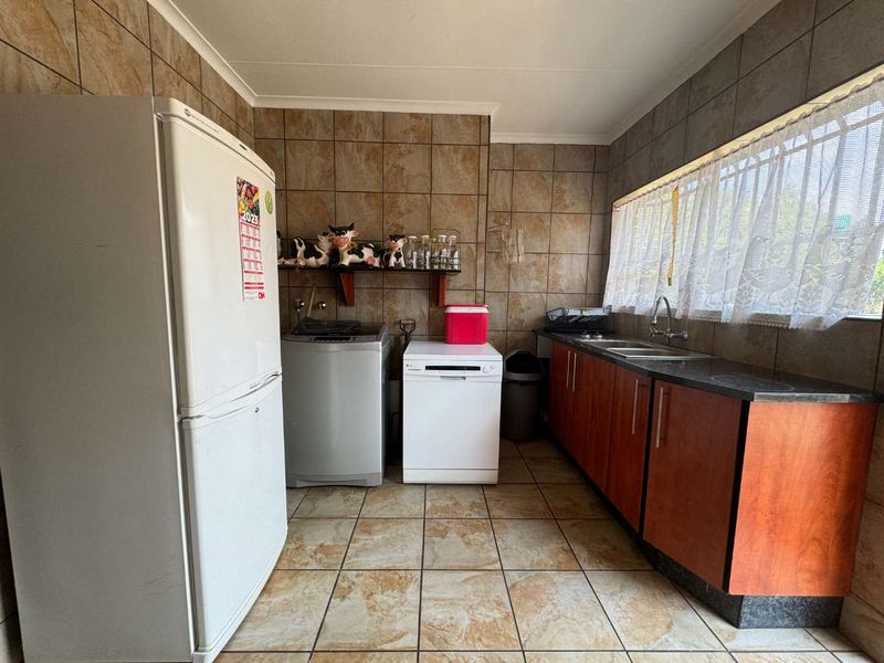 A functional laundry room featuring tiled walls and floors, built-in cabinetry, and a stainless steel sink with plumbing connections for appliances.