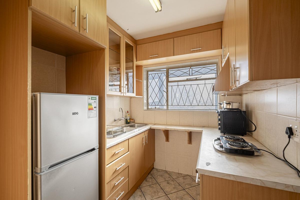 A compact kitchen featuring light wood-tone cabinetry, tiled backsplash, and a functional layout with a stainless steel sink and window for natural light.