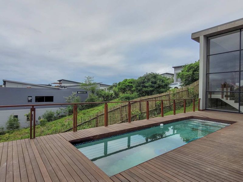 Outdoor pool area featuring timber decking, a modern swimming pool, and a large glass facade overlooking the surrounding landscape.