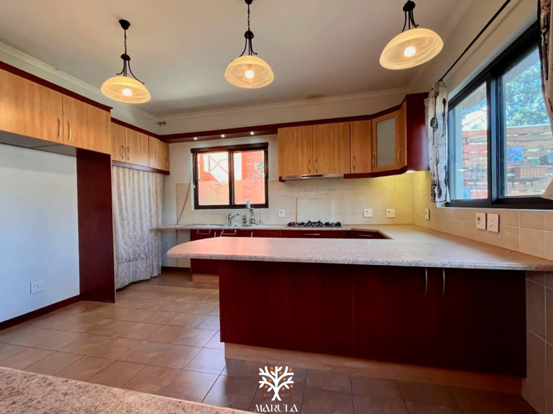 Spacious kitchen featuring built-in cabinetry, laminate countertops, a gas hob with extractor, and tiled flooring, offering a functional layout for culinary activities.