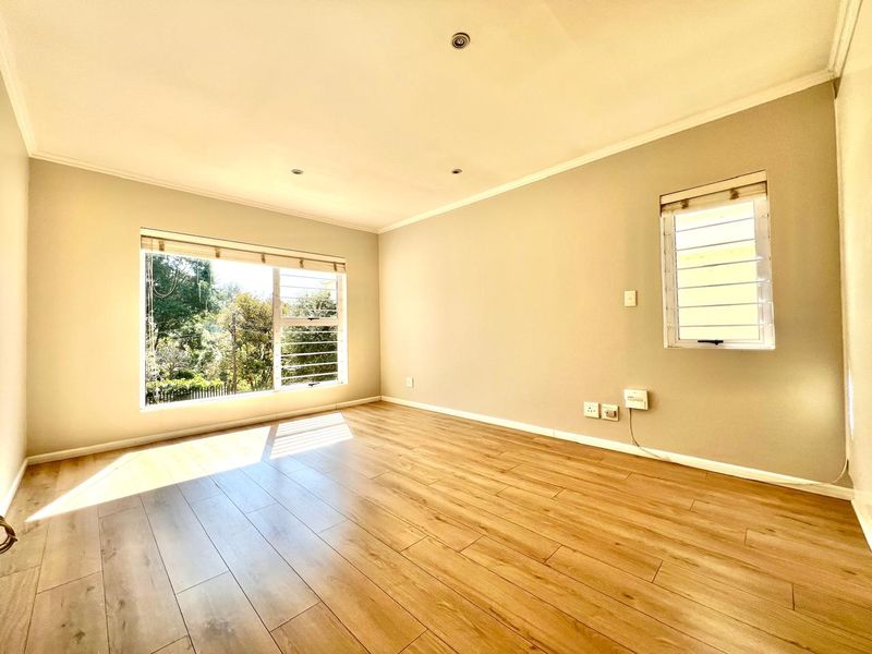 A bright and spacious empty living area featuring modern laminate flooring, recessed downlights, and large windows allowing for ample natural light.