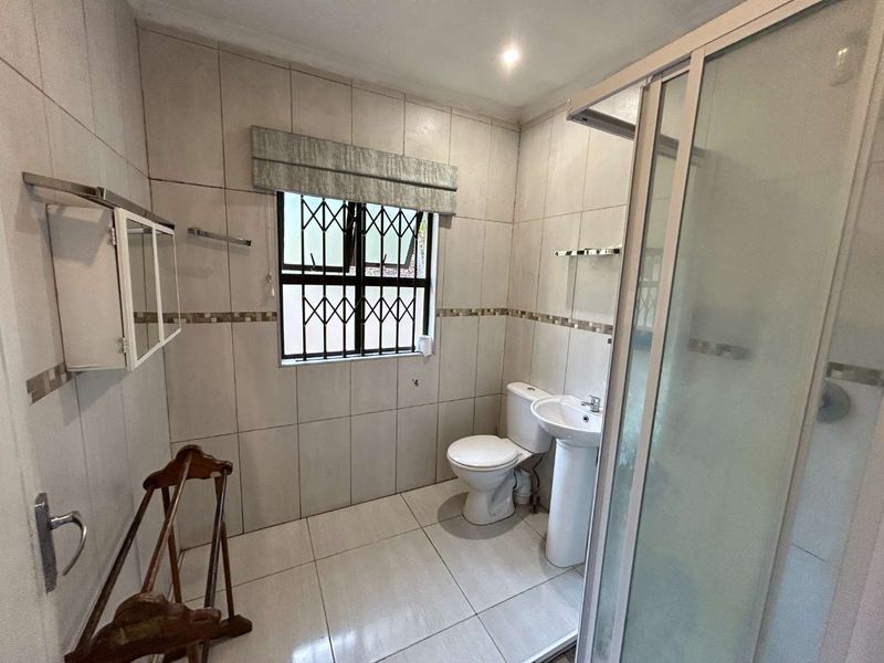 A functional bathroom featuring a pedestal basin, toilet, and a glass-enclosed shower with neutral wall and floor tiling.