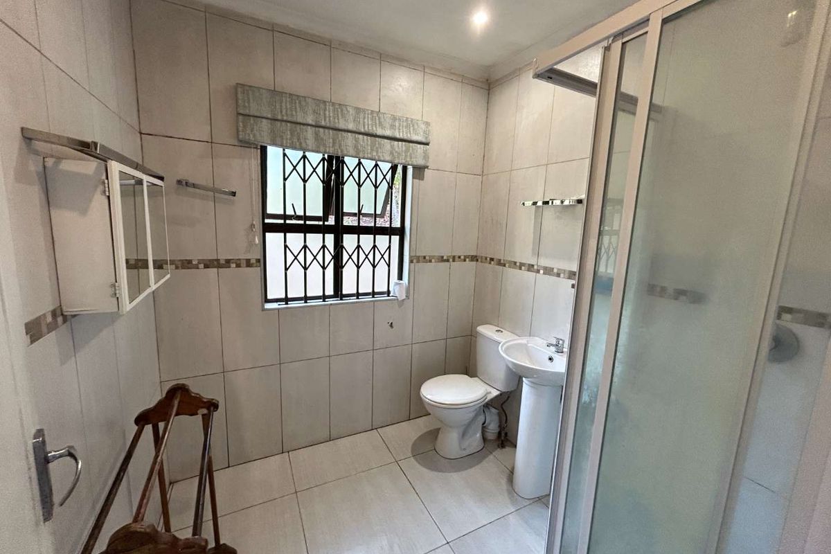 A functional bathroom featuring a pedestal basin, toilet, and a glass-enclosed shower with neutral wall and floor tiling.