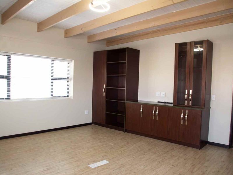 Spacious living area featuring exposed timber ceiling beams, laminate flooring, and extensive built-in dark wood cabinetry for storage and display.