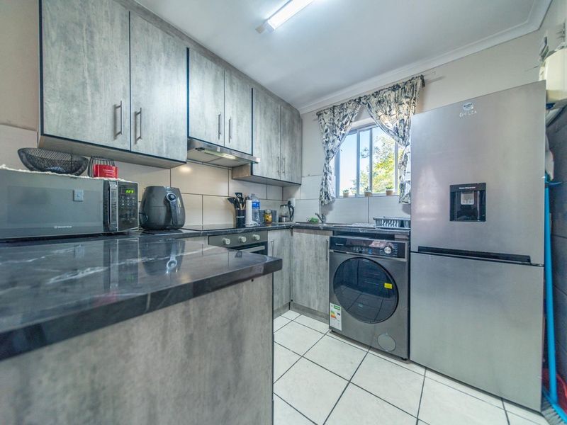 A functional kitchen featuring modern grey cabinetry, dark countertops, tiled flooring, and integrated appliances including a hob, oven, and extractor fan.