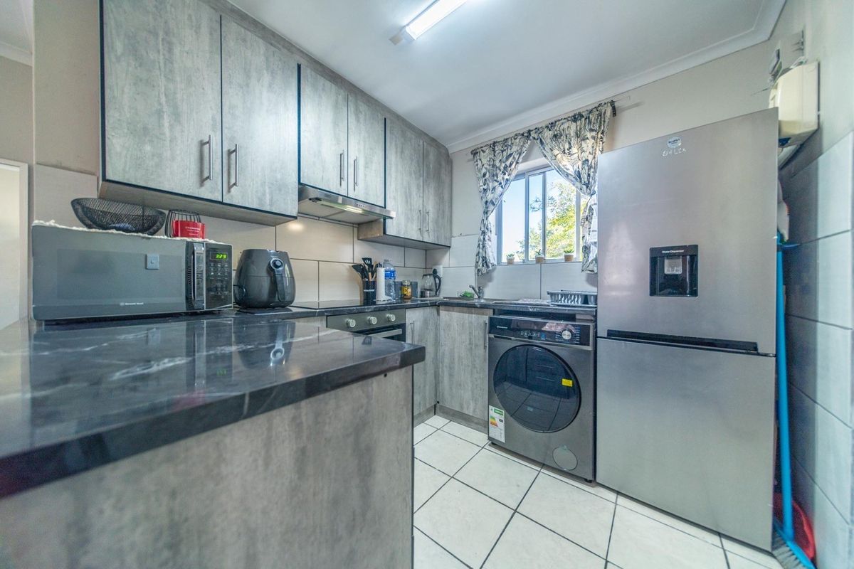 A functional kitchen featuring modern grey cabinetry, dark countertops, tiled flooring, and integrated appliances including a hob, oven, and extractor fan.