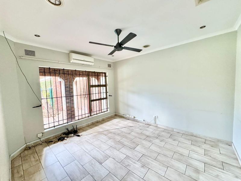 An empty living room featuring tiled flooring, a ceiling fan, and a split-system air conditioner, with security bars installed on the window.