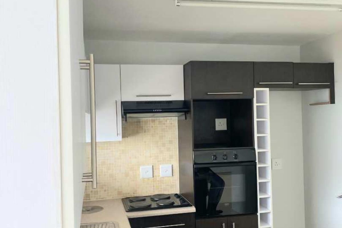 A functional kitchen featuring built-in oven, hob, extractor fan, double sink, and ample cabinetry with a dedicated wine rack.
