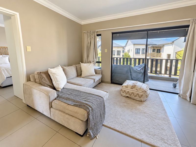 A bright living room featuring neutral tiled flooring, crown molding, and large sliding glass doors that open onto a private balcony.