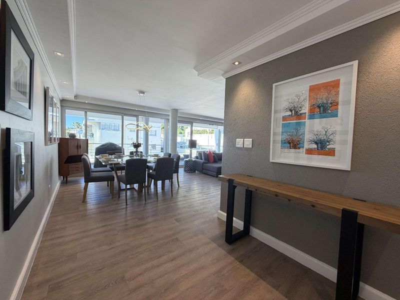 Spacious open-plan living and dining area featuring modern laminate flooring, recessed lighting, crown molding, and large sliding glass doors leading to an outdoor space.