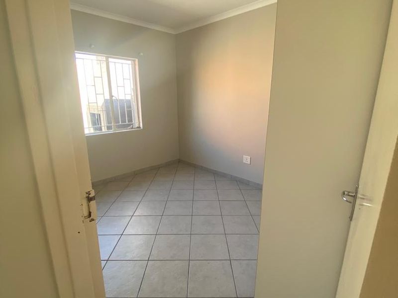 A bright, empty bedroom featuring neutral wall paint, tiled flooring, and a window fitted with security bars.