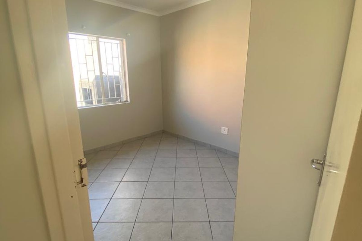 A bright, empty bedroom featuring neutral wall paint, tiled flooring, and a window fitted with security bars.