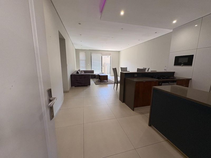 Modern open-plan living area featuring a sleek kitchen with built-in appliances, stone countertops, and large format floor tiles leading to a bright lounge space.