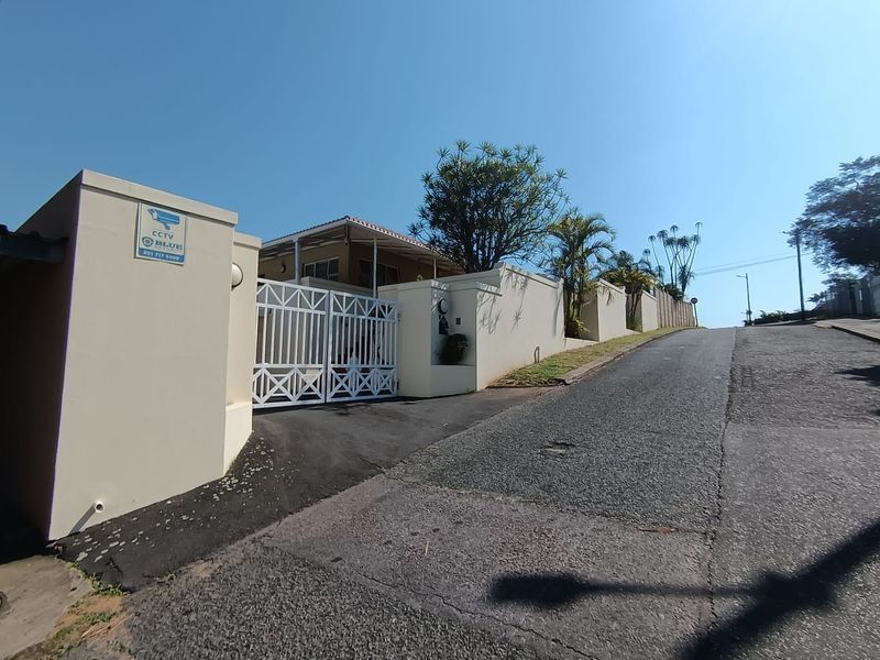 Front exterior view of the property featuring a secure perimeter wall, gated entrance, and paved driveway access from the street.