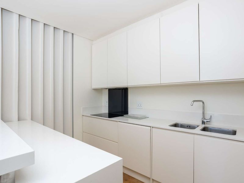 Modern minimalist kitchen featuring sleek white cabinetry, integrated hob, stone countertops, and a double stainless steel sink with a contemporary mixer tap.