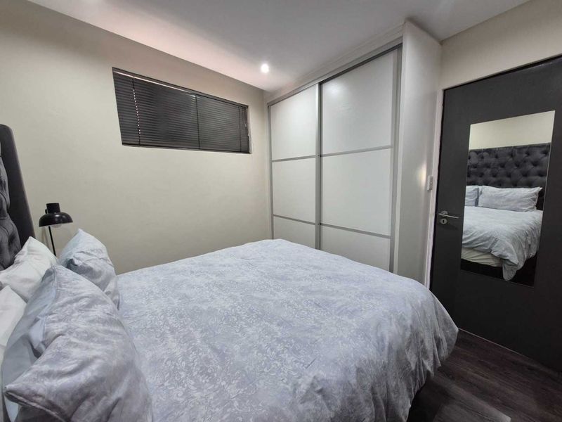 A well-maintained bedroom featuring modern laminate flooring, recessed downlighting, and a large built-in sliding door wardrobe.