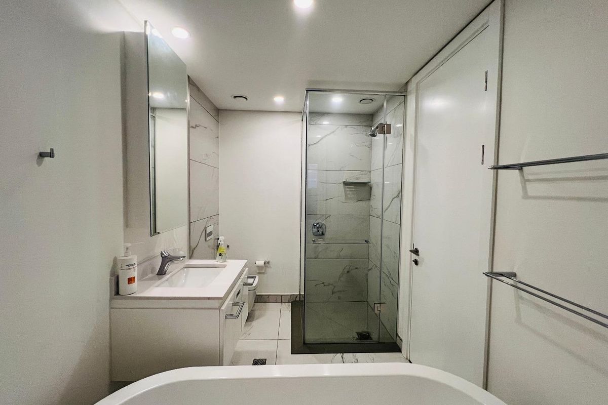 Modern bathroom featuring a glass-enclosed shower, vanity with integrated basin, and a freestanding bathtub, finished with marble-look wall tiles and recessed lighting.