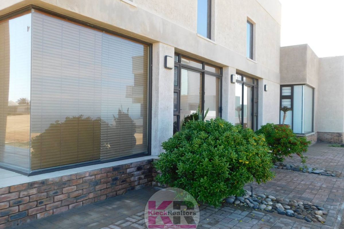 A modern exterior view of the property featuring large glass windows, brick base detailing, and paved outdoor areas.