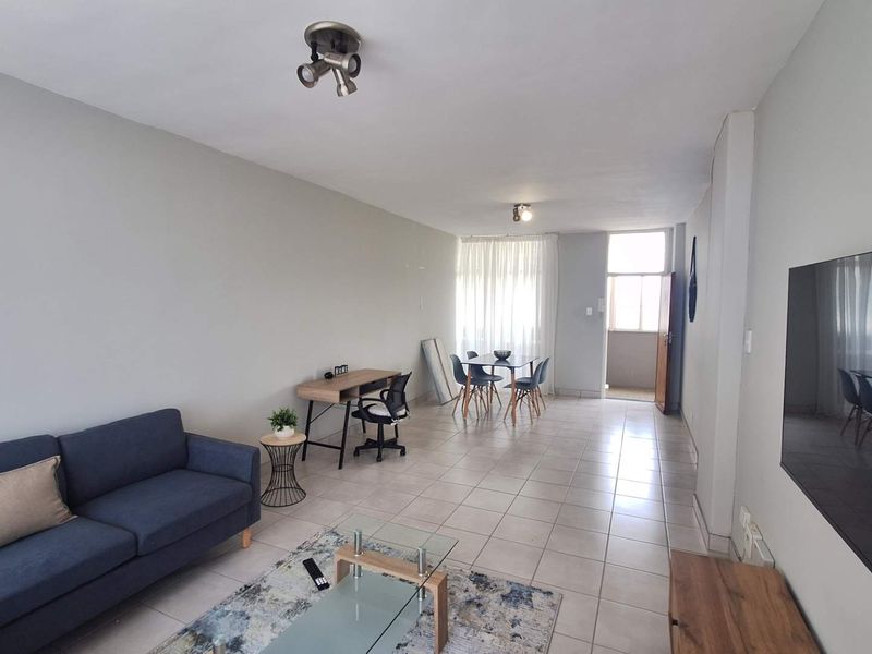 Spacious open-plan living and dining area featuring neutral wall finishes, tiled flooring, and direct access to a balcony through a sliding glass door.