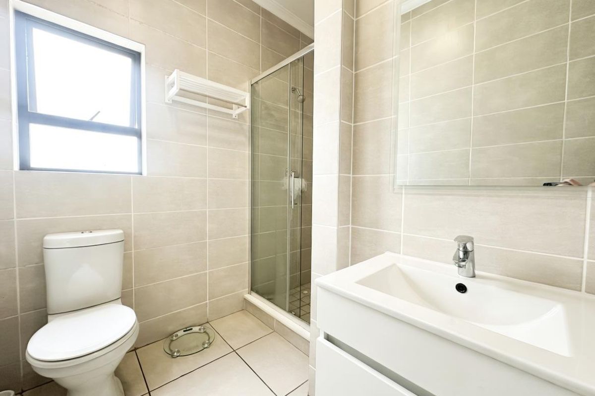 Modern bathroom featuring a glass-enclosed shower, wall-mounted vanity with basin, mirror, and neutral floor-to-ceiling tiling.