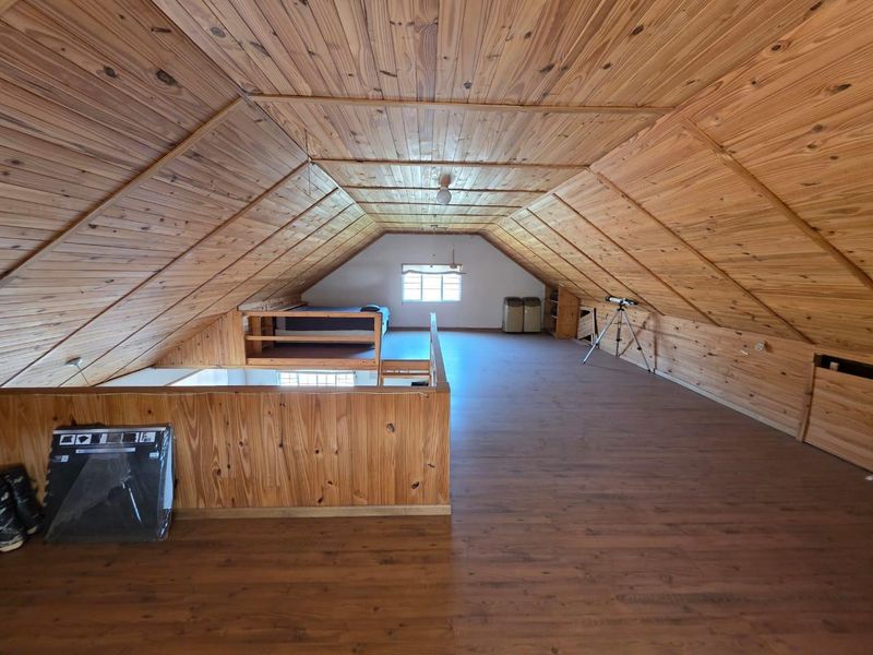 Spacious loft-style bedroom featuring extensive timber cladding on walls and vaulted ceilings, laminate flooring, and a mezzanine level overlooking the lower area.