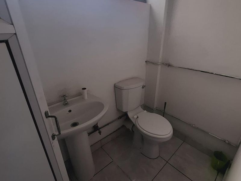 A compact bathroom featuring a pedestal basin and toilet with tiled flooring and visible surface-mounted plumbing.