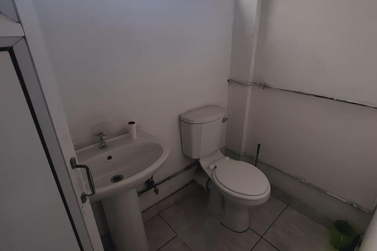 A compact bathroom featuring a pedestal basin and toilet with tiled flooring and visible surface-mounted plumbing.