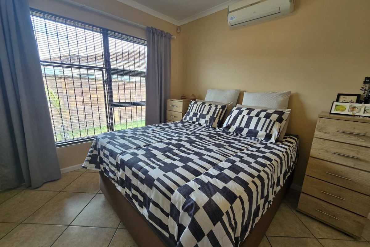 A bedroom featuring tiled flooring, a large window with blinds, and a wall-mounted air conditioning unit.