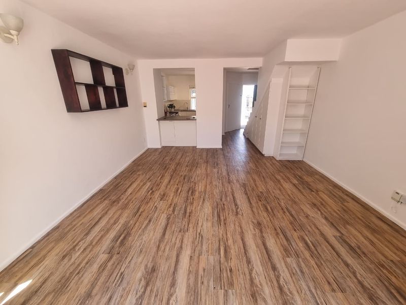An open-plan living area featuring wood-look laminate flooring, neutral walls, and a pass-through opening to the kitchen, providing a bright and versatile living space.