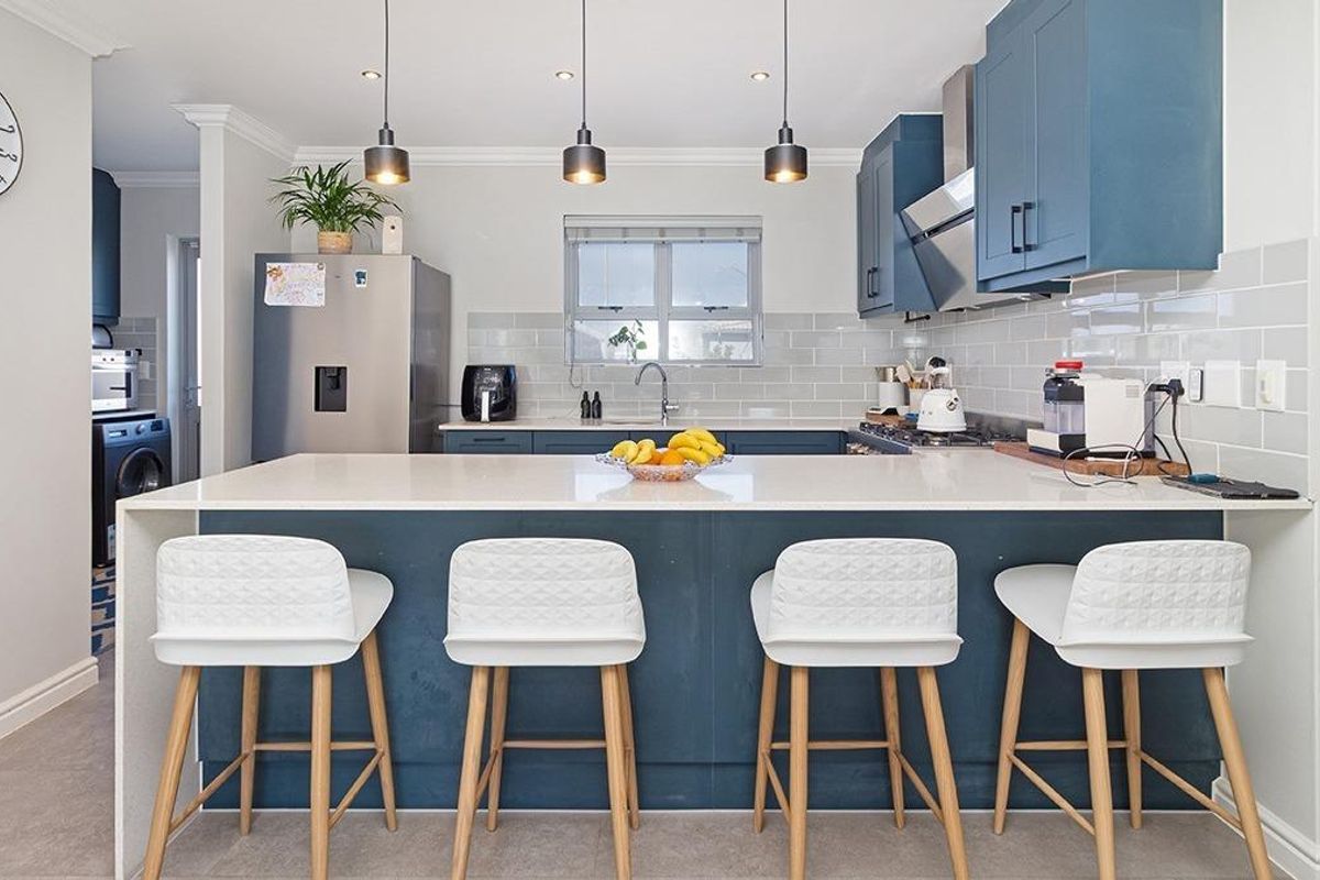 Modern kitchen featuring blue cabinetry, a central island with stone countertop, subway tile backsplash, and integrated stainless steel extractor fan.