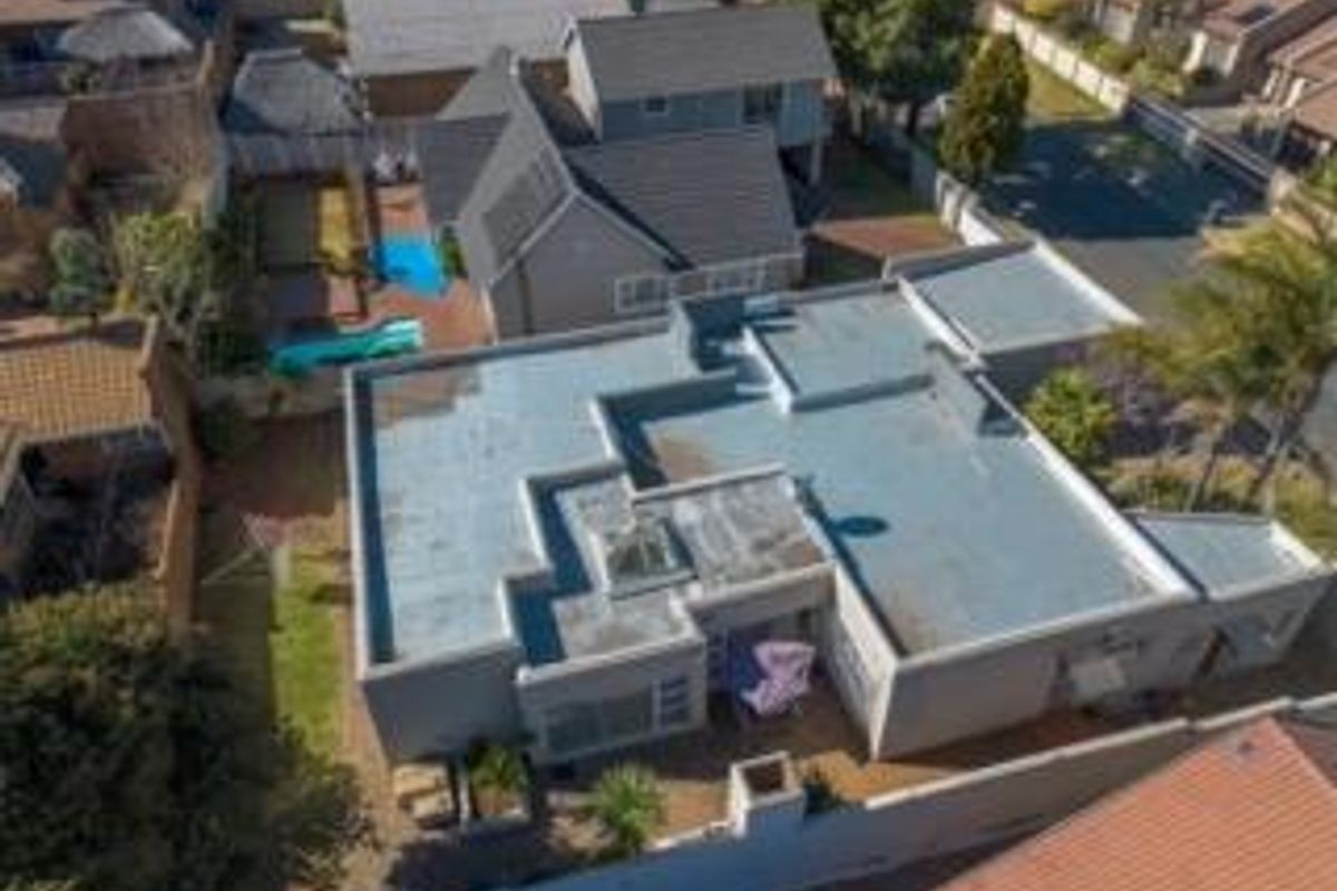 Aerial view of the property showcasing the flat and pitched roof structure, swimming pool, paved patio area, and surrounding boundary walls.